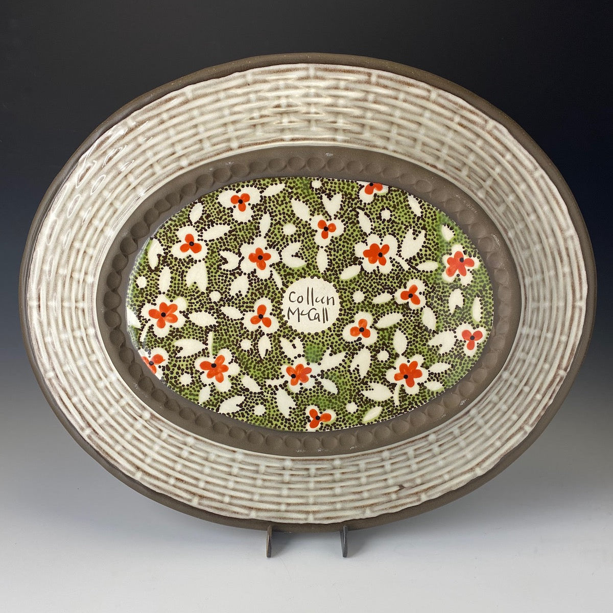 Decorative plate with floral pattern and artist's signature on a stand against a dark background