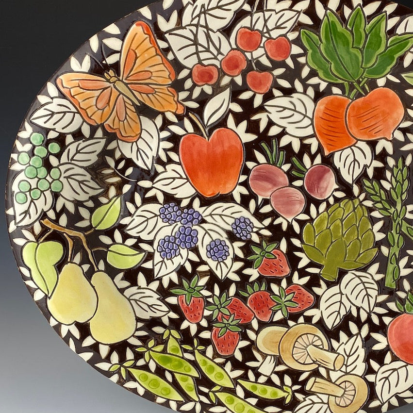 Decorative plate with colorful fruit, butterfly, and leaf pattern on a dark brown background
