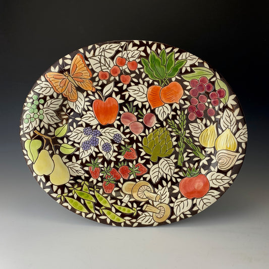 Decorative ceramic platter with colorful fruit, vegetable, and butterfly design on a dark background